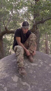 Young Native American man ties his shoe on a boulder and then hops off past the camera. Camera angle is straight on. Vertical handheld.