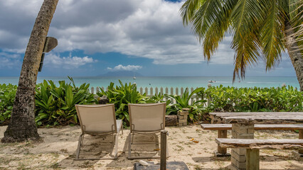 A relaxation area on a tropical beach. On the sand under the palm trees there are sun loungers,...
