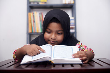 Little girl praying and reading Koran at home