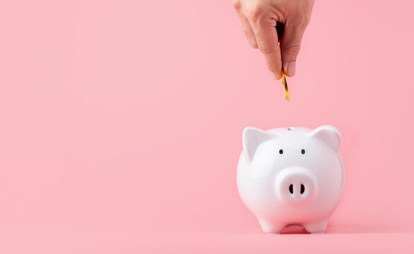 Money saving and investment concept. Hand putting coin to piggy bank on pink background with copy space