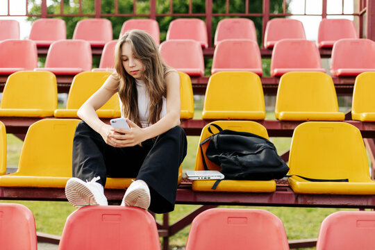 A teenage girl sits on the school bleachers and writes a message on her phone in her free time