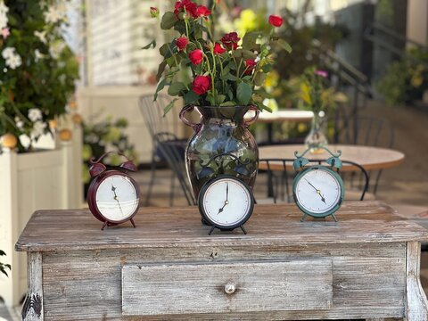 Clock and flowers on the table. A bouquet of red roses in a vase and alarm clocks showing different times on an antique wooden table in an old cafe.