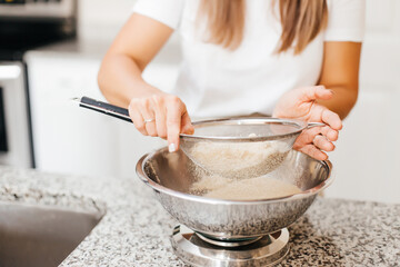 Fototapeta na wymiar A young beautiful woman cooks in a bright kitchen. Cooking macaroons. A cute girlp repares dough for cakes, hands and ingrident closeup. Cooking macaroons. Cookie baking