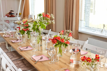 Glasses, forks, knives, napkins and a decorative flower on a dark brown wooden table served for dinner in a cozy restaurant