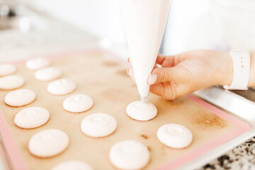 Obraz na płótnie Canvas A young beautiful woman cooks in a bright kitchen. Cooking macaroons. A cute girlp repares dough for cakes, hands and ingrident closeup. Cooking macaroons. Cookie baking
