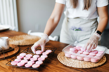 Obraz na płótnie Canvas Female hands and two halves of pink macaroons with stuffing close-up. Cookie baking. Macaroons making