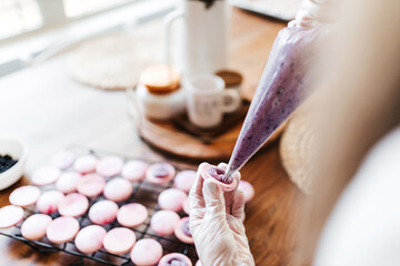Female hands and two halves of pink macaroons with stuffing close-up. Cookie baking. Macaroons...