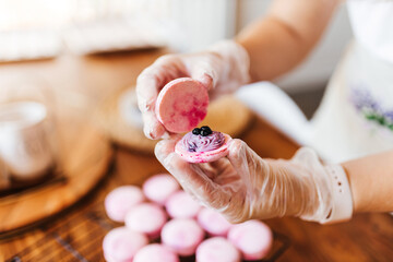Female hands and two halves of pink macaroons with stuffing close-up. Cookie baking. Macaroons...