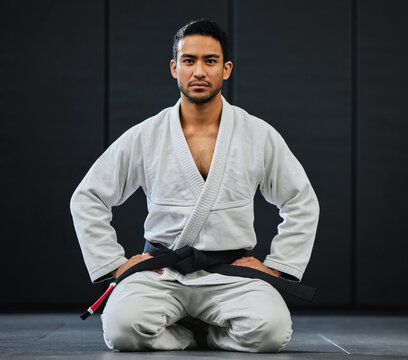 . Male coach ready for karate training at fitness studio, looking serious at dojo practice in gym and sitting on the floor at a self defense class. Portrait of tough, healthy and active trainer.