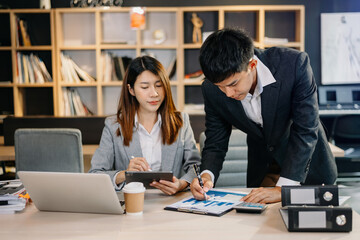 Asian business colleague business presents and explains and using laptop and tablet. Teamwork, financial marketing team,   while sitting in modern office room..