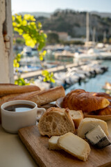 French breakfast with fresh baked croissants, baquett bread, crottin goat cheese, black coffee and view on fisherman's boats in harbour of Cassis, Provence, France