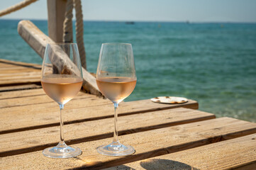 Glasses of cold rose wine from Provence served outdoor on wooden yacht pier with view on blue water and white sandy beach Plage de Pampelonne near Saint-Tropez, France