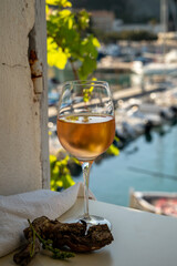 Cold rose wine in glass served on outdoor terrace in sunlights with view on old fisherman's harbour with colourful boats in Cassis, Provence, France
