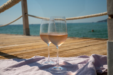 Glasses of cold rose wine from Provence served outdoor on wooden yacht pier with view on blue water and white sandy beach Plage de Pampelonne near Saint-Tropez, France