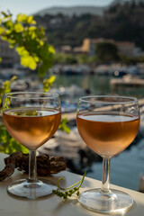 Cold rose wine in glasses served on outdoor terrace in sunlights with view on old fisherman's harbour with colourful boats in Cassis, Provence, France