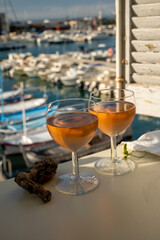 Cold rose wine in glasses served on outdoor terrace in sunlights with view on old fisherman's harbour with colourful boats in Cassis, Provence, France