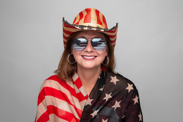 Beautiful middle aged 40+ 50+ patriotic woman smiling looking at camera wearing flag hat shirt and sunglasses