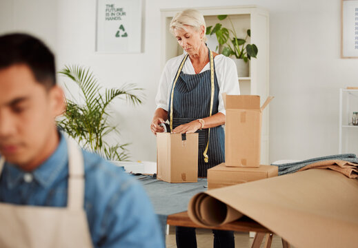 . Fashion, design and style with a tailor, seamstress or creative designer packing boxes for shipment and delivery. Female stylist preparing a box to complete an order in her studio or workshop.
