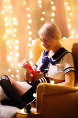 Blonde woman in sexy anime costume unpacks gift box with red christmas bow