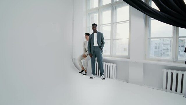 Two men in business suits posing by the window in a white studio