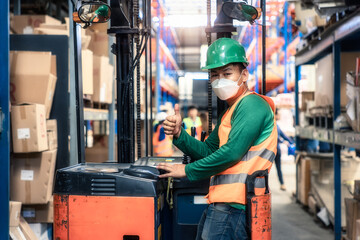 Fototapeta na wymiar Portrait of forklift operator with thumb in distribution warehouse. May called industrial worker, driver, asian man or person. To wear safety helmet, vest, mask. Concept for job, training, occupation.