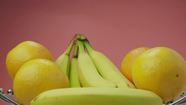 Bananas and oranges on a pink background. Rotating fruits.
