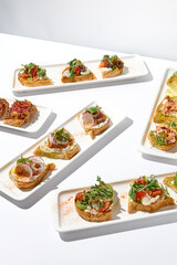 Aesthetic composition with bruschetta on white background over white wall. Set of bruschetta with shrimp, salmon, beef, tomatoes and crab on fine dining in summer. Elegant menu concept.