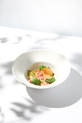Elegant salad with crab meat, espuma sauce and lettuce on white table with harsh shadows. Green salad with crab and creamy sauce in summer menu. Aesthetic food. Seafood appetizer.