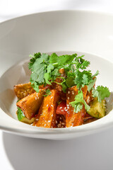 Crispy eggplant in chinese style on white plate. Crispy eggplant salad on summer menu. Asian appetizer - roasted aubergine with coriander leaves. Vegan food. Aesthetic veggie menu.