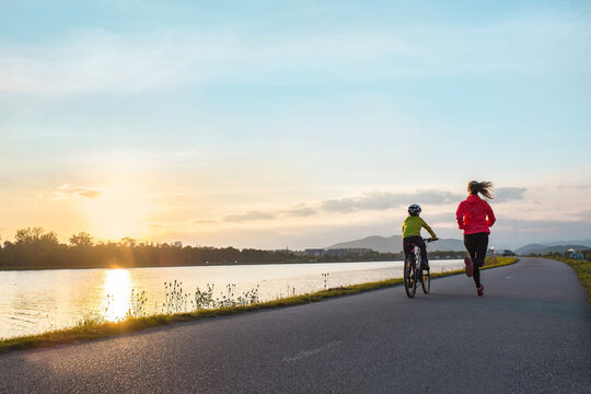 Happy mother and son go in sports outdoors. Boy rides bike in helmets, mom runs on sunny day. Silhouette family at sunset. Fresh air. Health care, authenticity, sense of balance and calmness