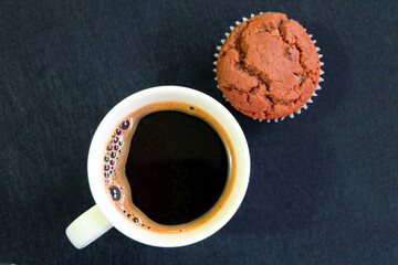 Cup of coffee and cupcake on dark background.