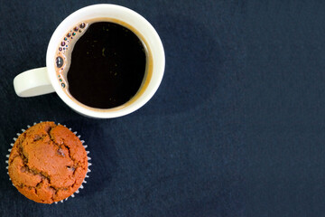 Cup of coffee and cupcake on dark background.