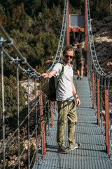 Traveler with a backpack in the mountains. A middle-aged man stands on a suspension bridge on a...