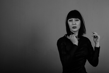 A beautiful girl with dark hair in a black dress poses on a dark