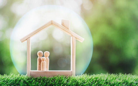 Wooden Home With Happy Family Of Wooden Doll Is Placed Inside On Nature Bokeh. The Saving Money For House Or Real Estate Owner In The Future Concept. Stay Safe At Home Concept For Coronavirus COVID 19