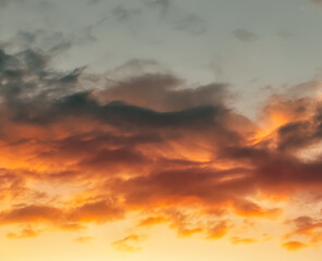 Dramatic sunset landscape with puffy clouds lit by orange setting sun and blue sky.