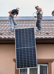 Men workers lifting up photovoltaic solar modul on roof of house. Electricians in helmets installing solar panel system outdoors. Concept of alternative and renewable energy. © anatoliy_gleb