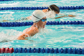 Boy swimming Butterfly in a race. Focus on face and water drops, some motion blur. Professional swimmer, swimming race, indoor pool