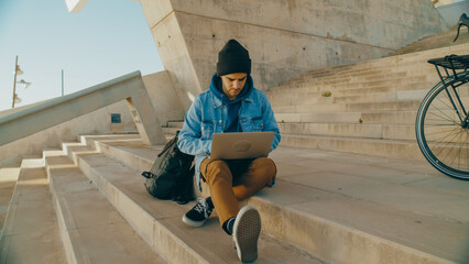 Portrait of student work on laptop outside, type code or text for new idea project. Young freelance worker work remote from office in park or urban area. Concentrated on work. Commuter with bicycle