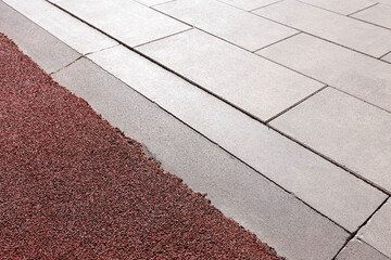 A sports surface made of crumb rubber adjoins the track with paved concrete tiles. Angle view. Selective focus.