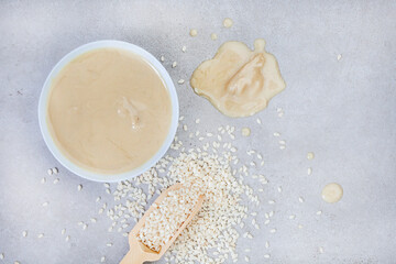 Pure sesame tahini with sesame seeds on mottled grey with copy space