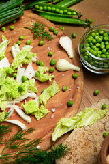 vegetables on a wooden kitchen board, green onions, dill and peas, sliced cabbage on a wood background, concept of fresh and healthy food, still life