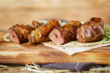 A roll or sausage made of meat with grilled liver lies on a wooden board and hay. The concept of restaurant cuisine.