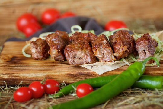 Grilled meat kebabs lie on a wooden board. Decorated with vegetables and thin bread. Food according to the cook's recipes.