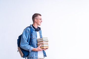 cheerful teenage with glasses, headphones, backpack and stack books in his hands stands against white wall. the smiling student looks away. emotional portrait beautiful teenage boy returning to school