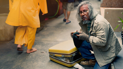 A homeless Asian man sits by the sidewalk asking for donations from passersby in despair with no...