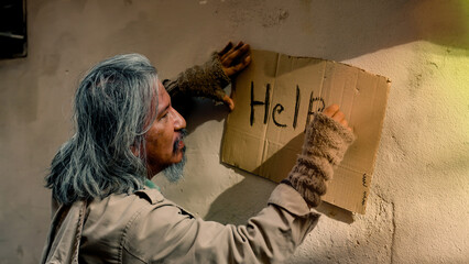 Close Up A homeless old man with long hair dressed in dirty clothes is writing a note on a piece of...