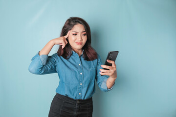 Tired thinking woman, has a sad expression while holding her smartphone. Isolated blue background