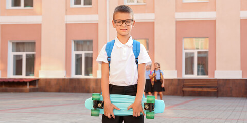 Cute schoolboy with skateboard outdoors