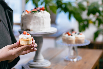 Pastry chef confectioner young caucasian woman holds cupcake in hands cake on kitchen table. Cakes cupcakes and sweet dessert
